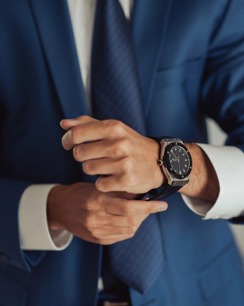 A man in a blue suit adjusting his cuff, wearing a dark wristwatch