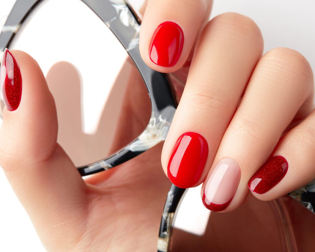A hand with red and nude nails reflected in a round mirror
