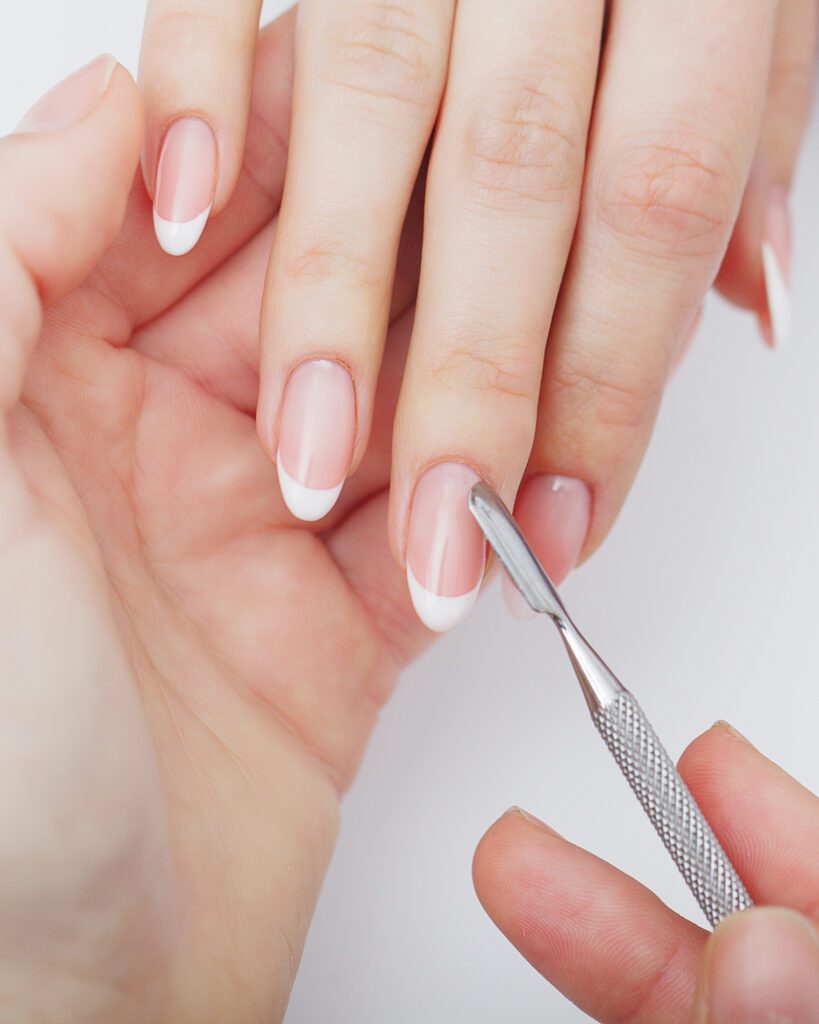 Cuticle pusher resting against almond nails with a soft white French tip