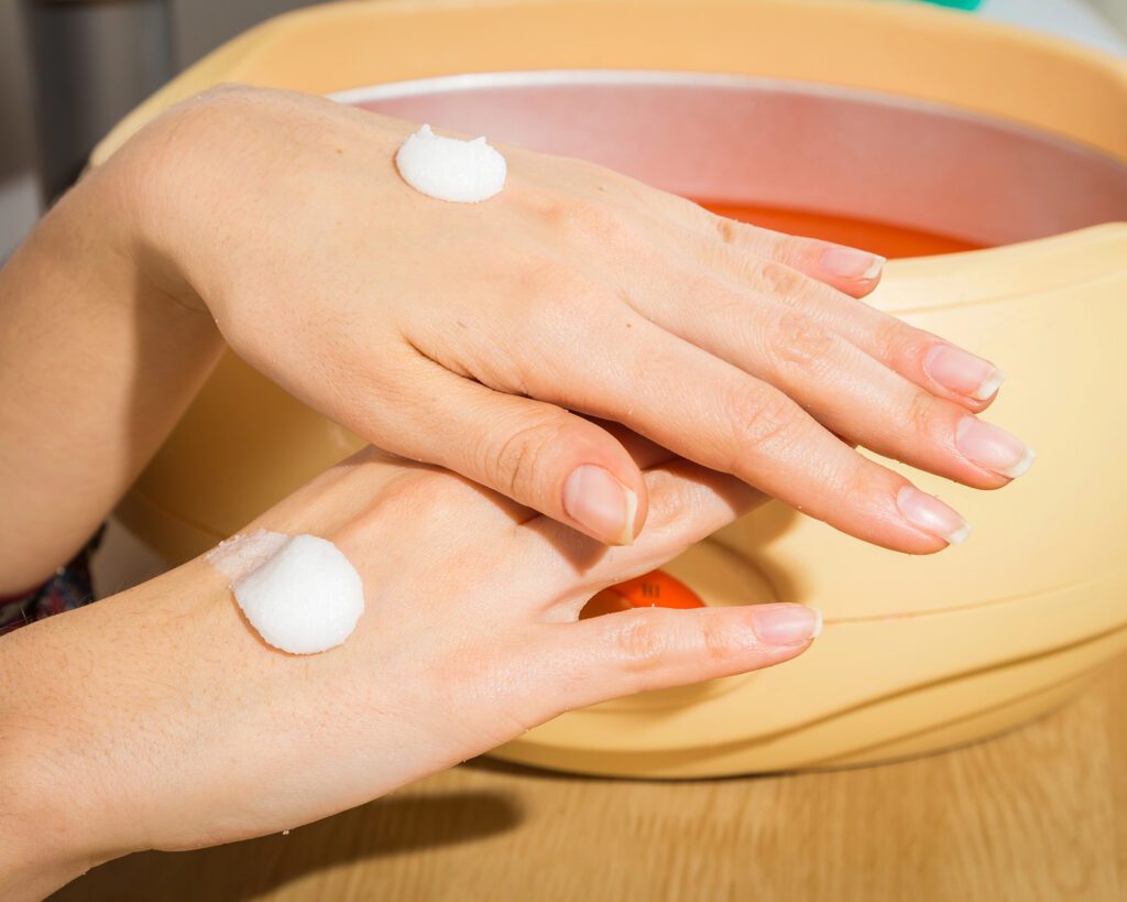 Two hands coated in white paraffin cream resting over a paraffin warmer