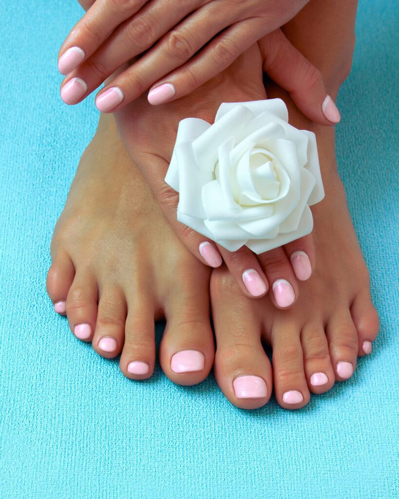 Hands and feet with pale pink nails on a turquoise surface, beside a white fabric rose
