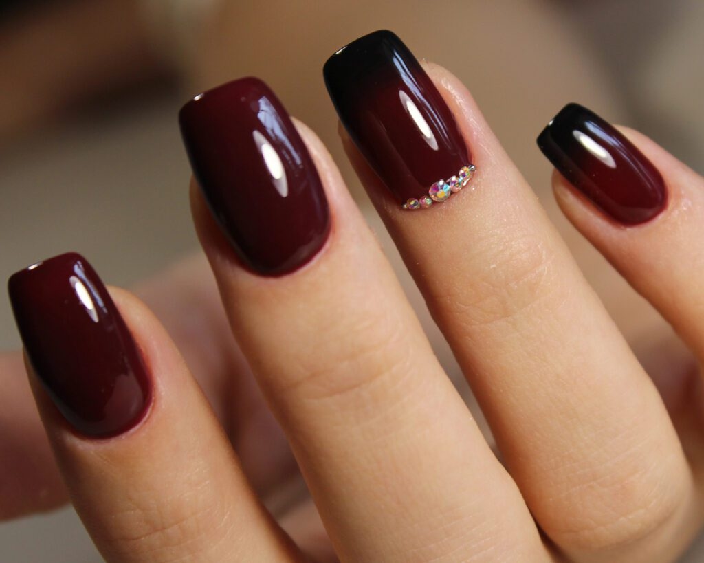Squared nails in glossy black-to-burgundy ombre gel with crystals along one accent nail
