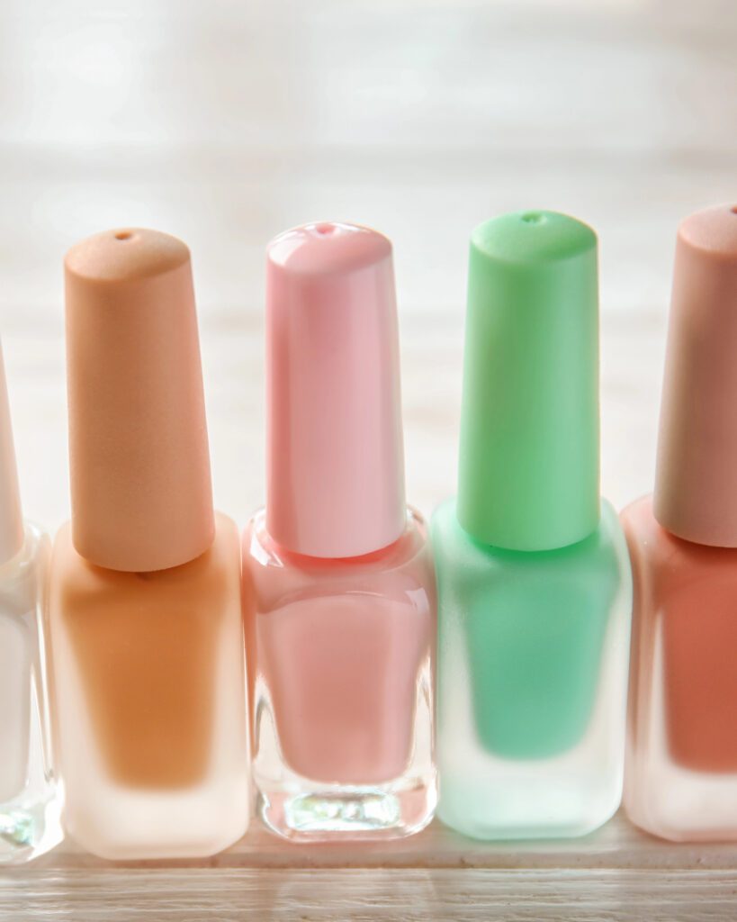 Row of pastel nail polish bottles in peach, pink and mint on a pale wooden surface