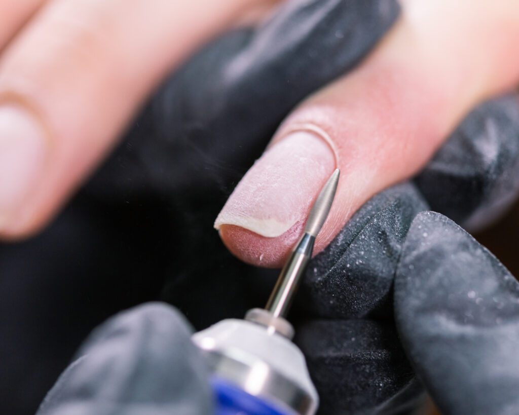 Close view of a rotary bit working across a nail surface, held in black gloved hands