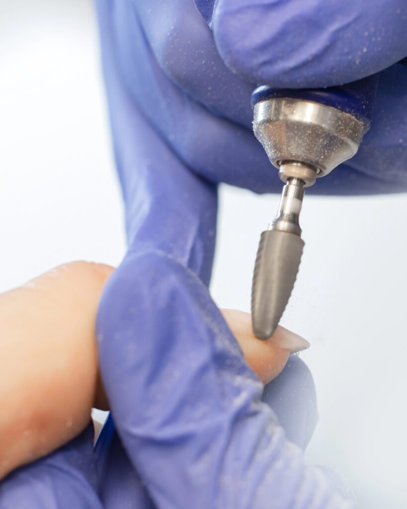 A technician in blue gloves using a wide rotary bit on a nail