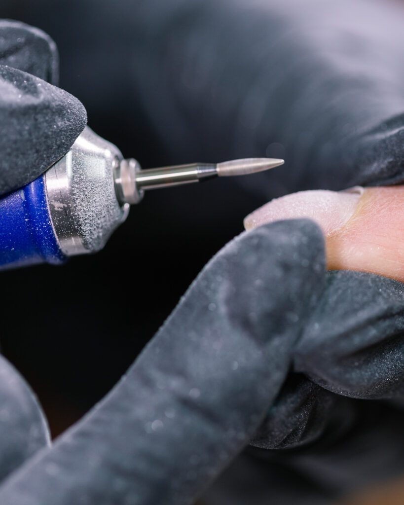 A rotary tool held in black gloves working on a bare nail, fine dust on the glove