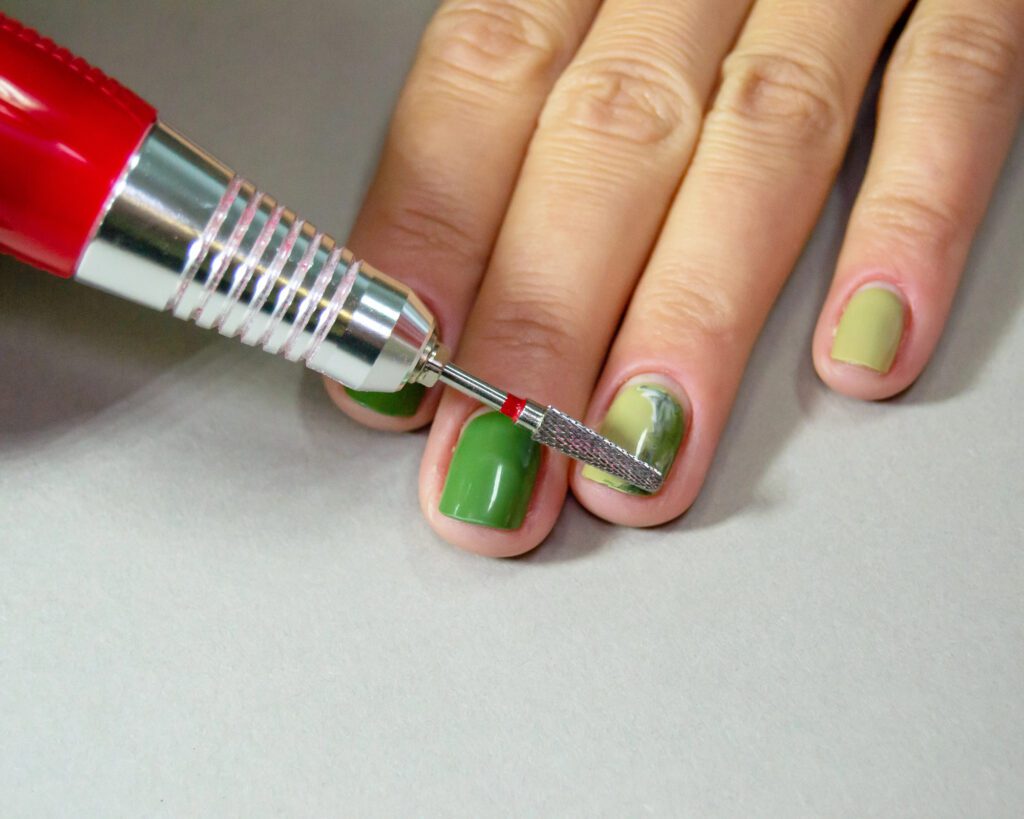 A red rotary handpiece filing across green polish on a nail