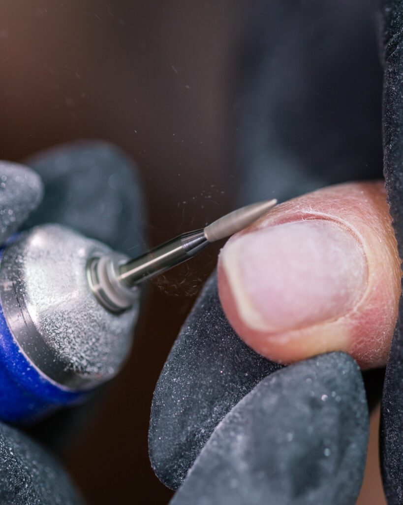 Close view of a rotary bit lifting polish from a nail, held in dark gloves