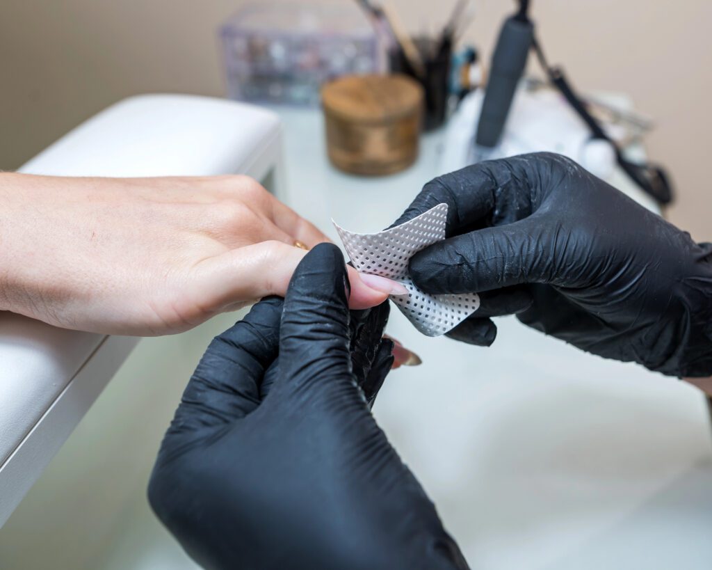 Technician in black gloves wrapping a nail with a foil removal pad at the manicure table