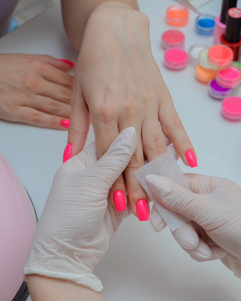 Technician in white gloves wiping a hand with neon pink square nails using a lint-free pad