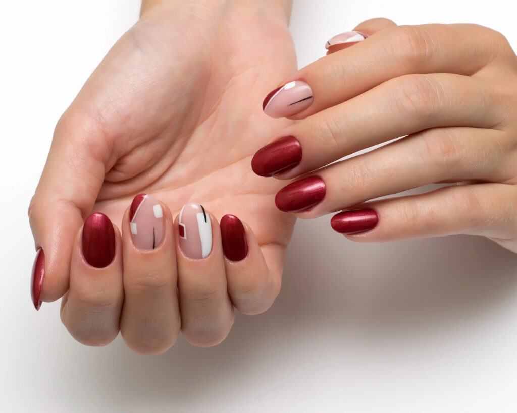 Two hands with deep red nails and one accent nail in white and nude line art