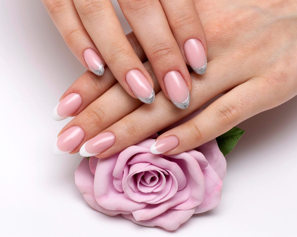 Two hands with pale pink nails and silver glitter French tips, resting on a lilac rose
