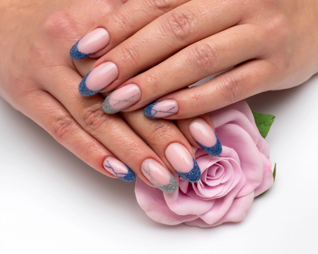 Two hands with nude nails and blue glitter tips with fine marbling, resting on a lilac rose