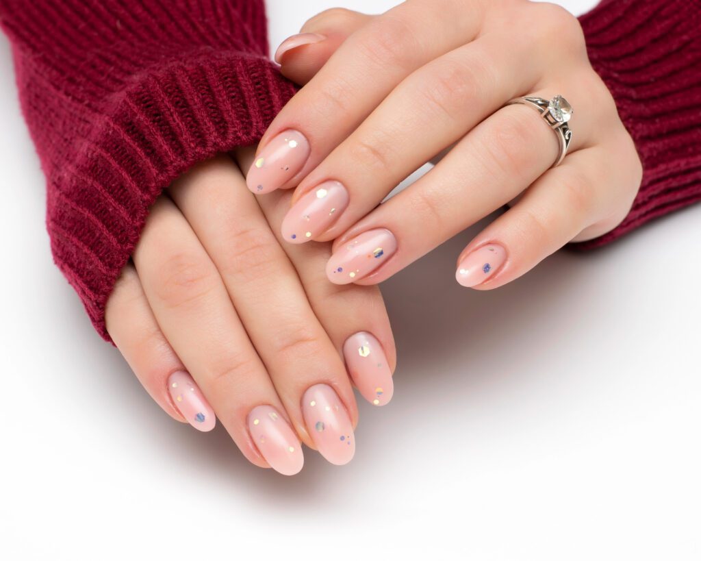 Two hands in a burgundy sweater with nude nails carrying small scattered dot accents