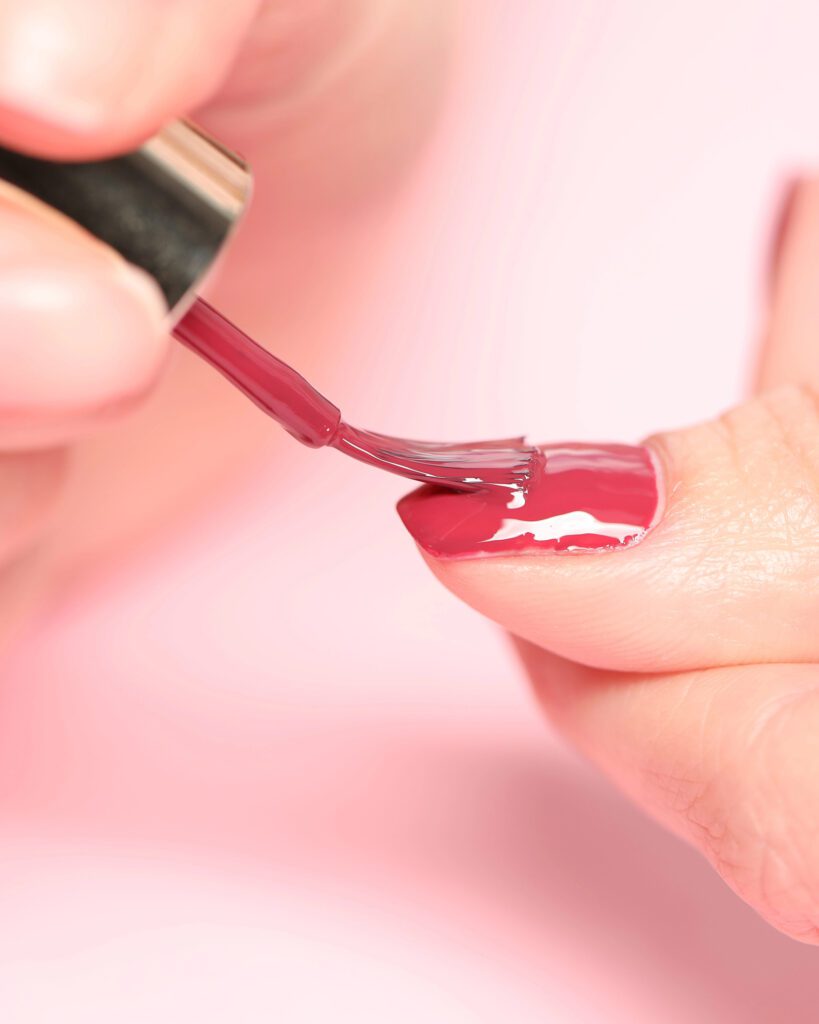 Close view of dark red polish being applied to a single nail against a pink background