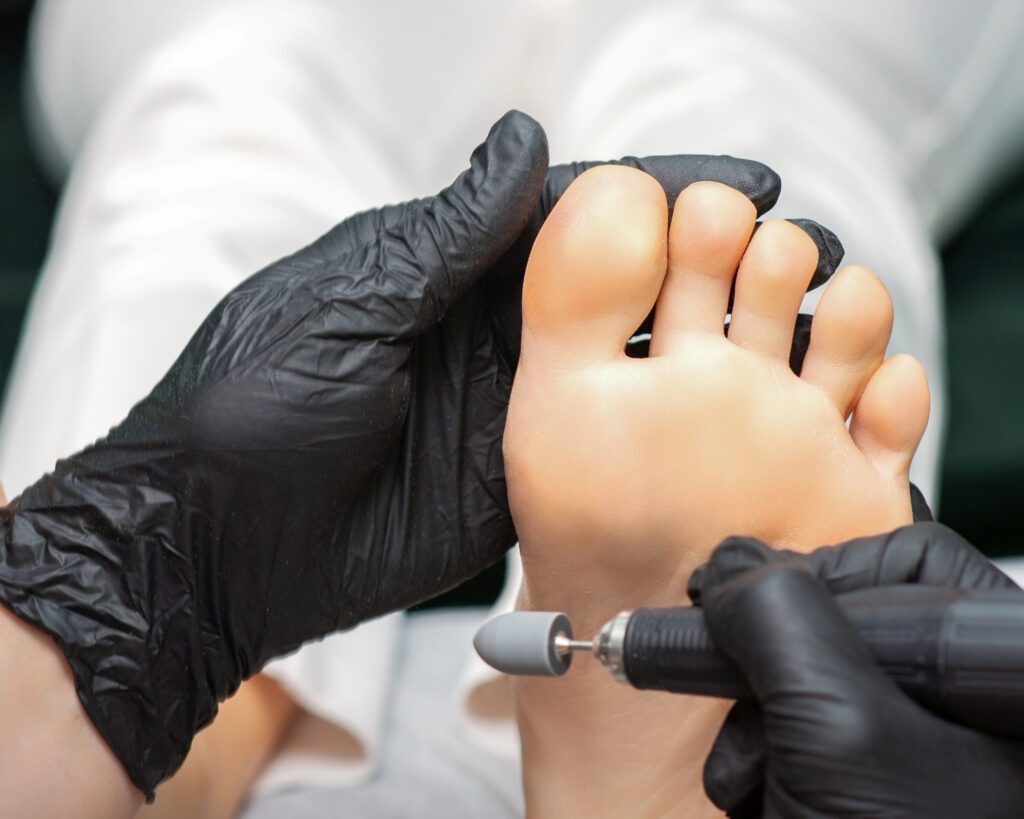 Technician in black gloves buffing the sole of a foot with a rotary pedicure attachment