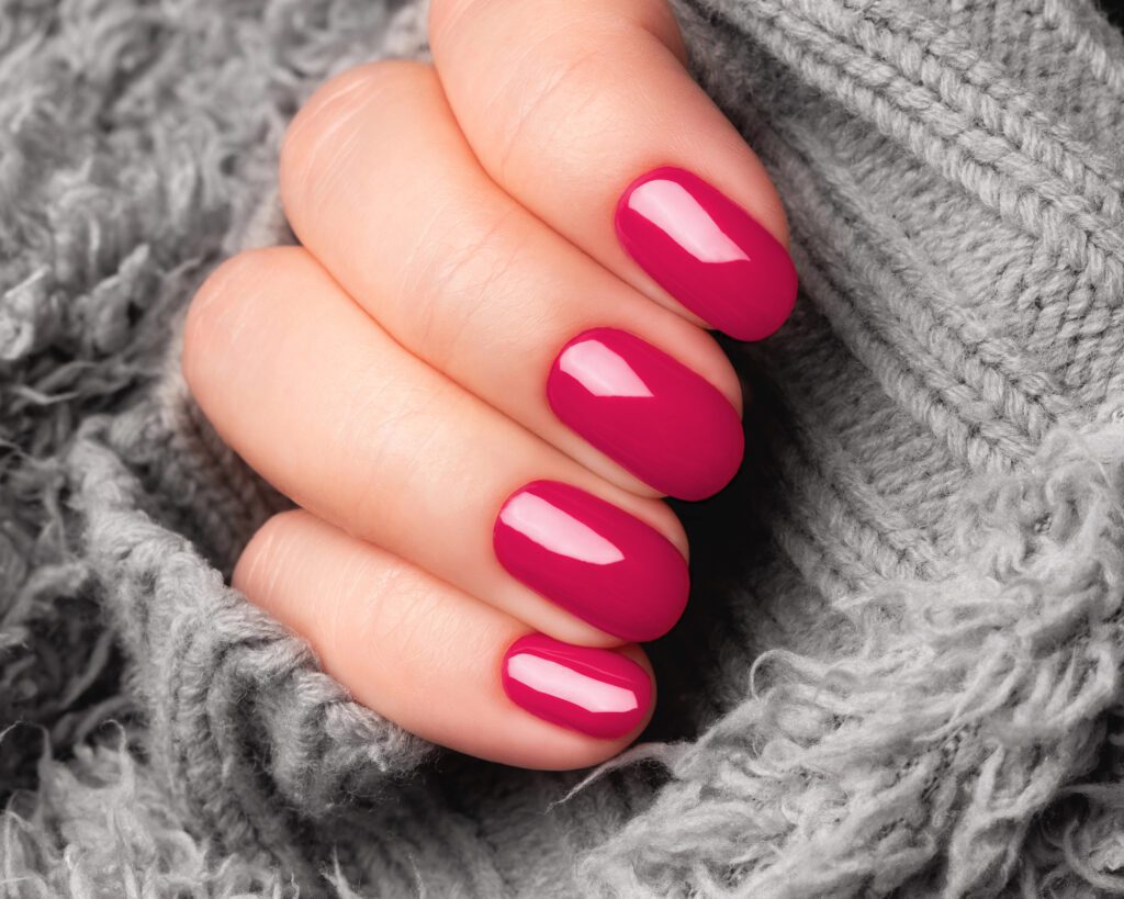 A hand with short square nails in a bright raspberry gloss, resting on grey knitwear