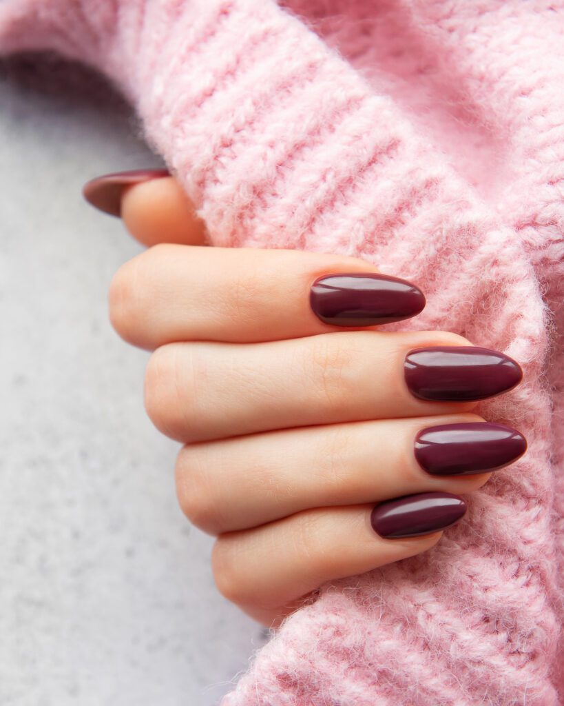 A hand in a pink knit sleeve with almond nails in a deep burgundy