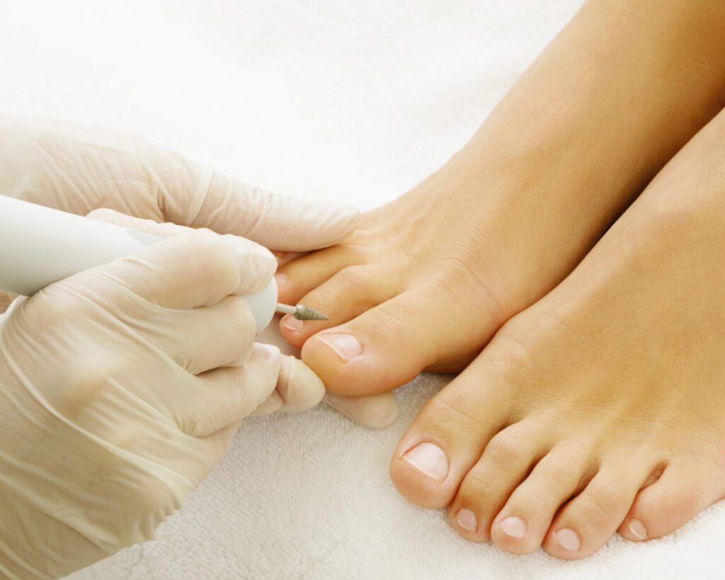 A gloved technician working on the toenails of a foot resting on a white towel