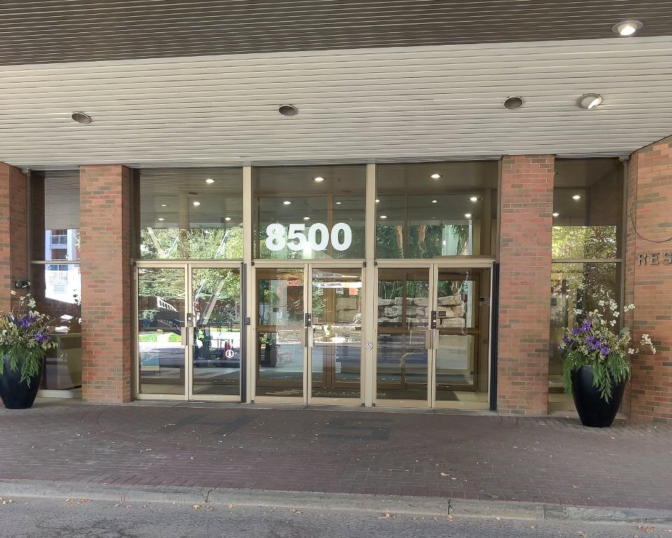 Glass entrance doors with the number 8500 above them and planters on either side.