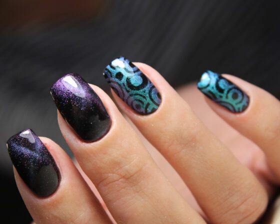 Close crop of hands against a dark blurred background, showing dark navy-violet shimmer nails with turquoise circle patterns on accent nails