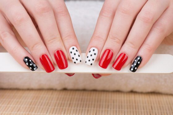 Close view of both hands above a pale woven surface, showing glossy red nails with black and white polka-dot accent nails