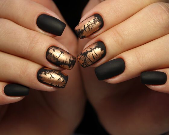 Close-up of two hands against a dark background, showing matte black nails alternating with distressed metallic gold accents