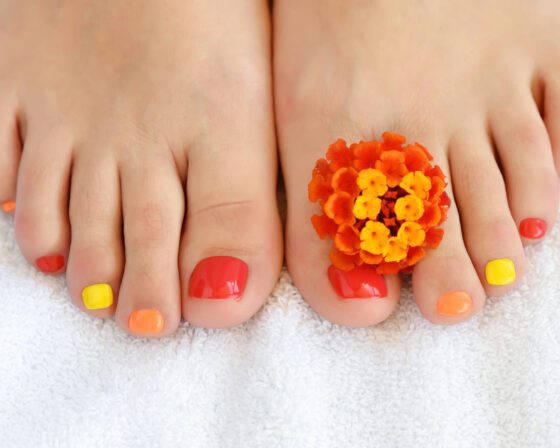 Close-up of toenails in red, orange and yellow with an orange flower between the toes