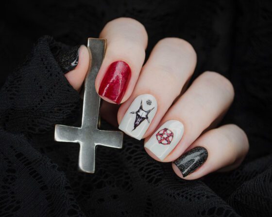 Short nails in red and black glitter with pale accents carrying dark gothic line art on black lace