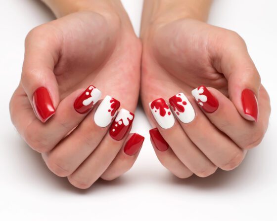 Cupped hands showing glossy red nails and white accents with red drip art