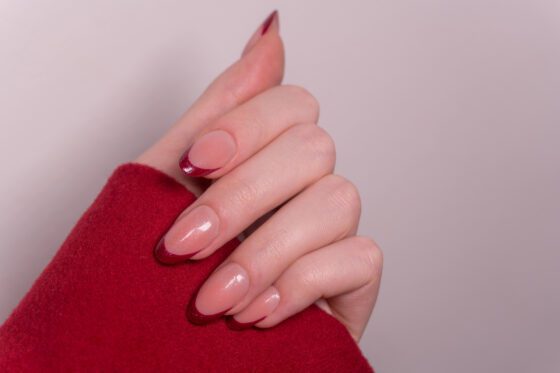 Close-up of curled hand against a muted gray background, showing medium blush almond nails with deep red French tips