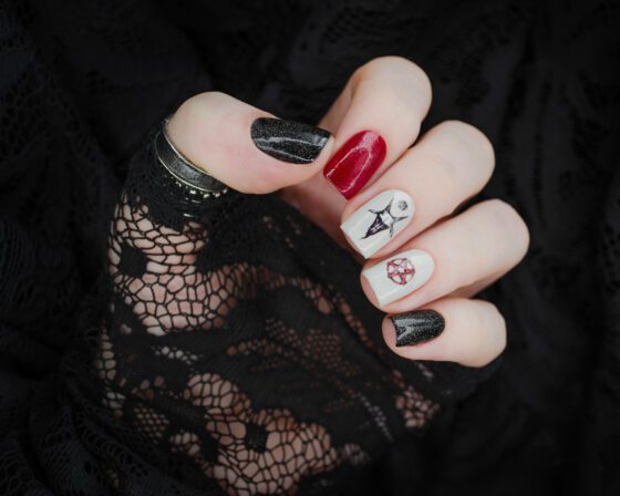 Hand on black lace showing red and black glitter nails and pale gothic line-art accents