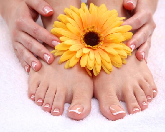 Feet with a nude French pedicure and white tips framing a yellow gerbera