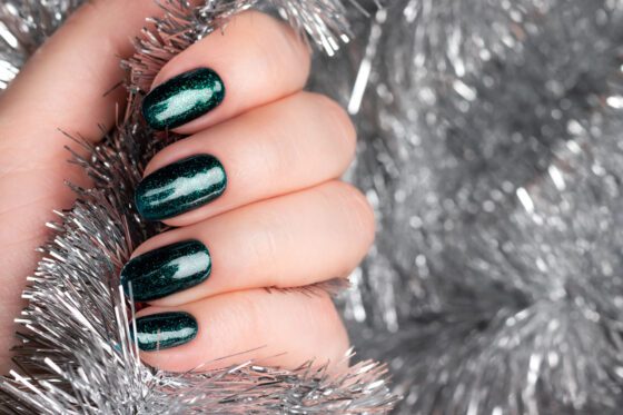 Macro close-up of hand amid silver tinsel, showing short nails in a deep teal green with fine sparkle