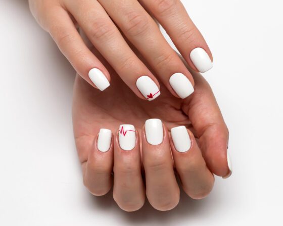 Symmetrical close-up of cupped hands on a white background, showing short white nails with a fine red heartbeat line and a small red heart on accent nails