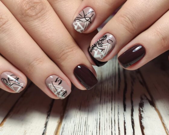 Horizontal close-up of two hands on pale wood, showing glossy deep plum nails with nude accents carrying black and white line art