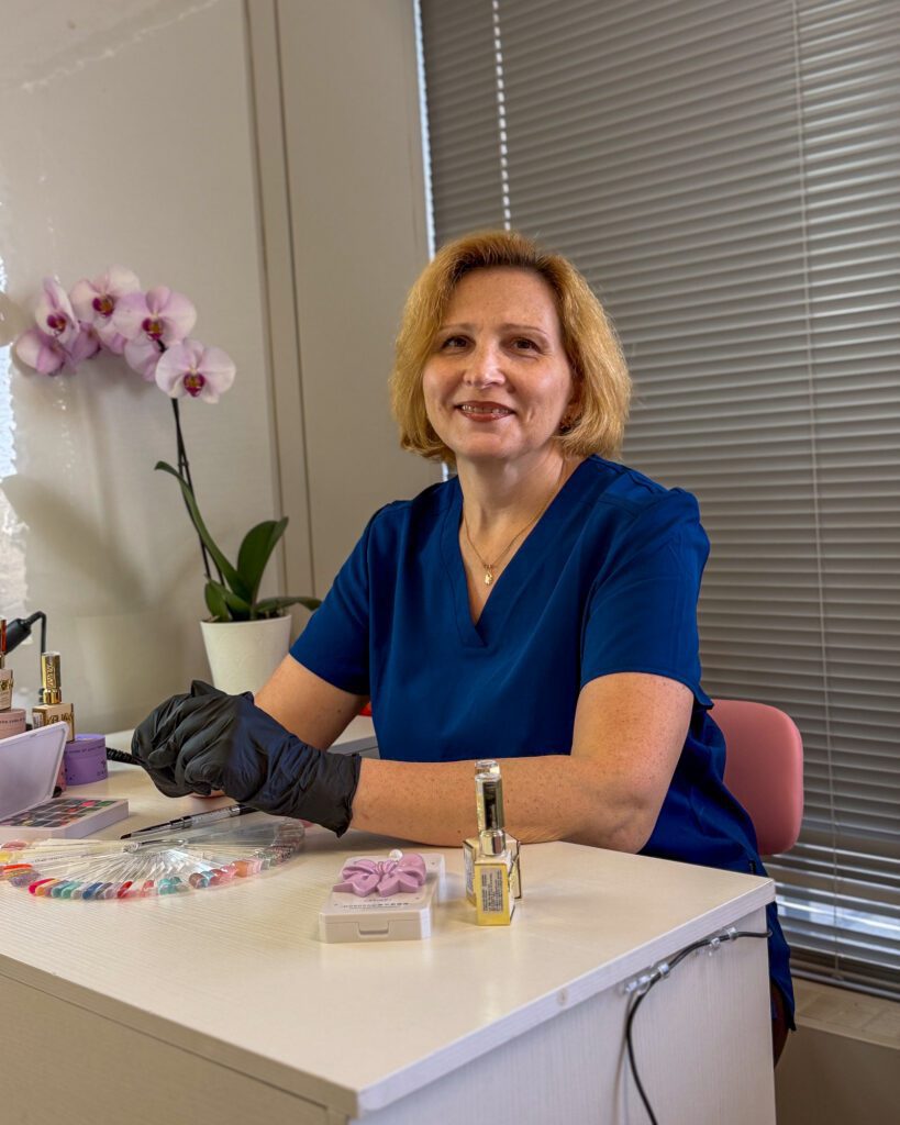 Olga Palamarenco smiling at her manicure table, in a navy uniform and black gloves.