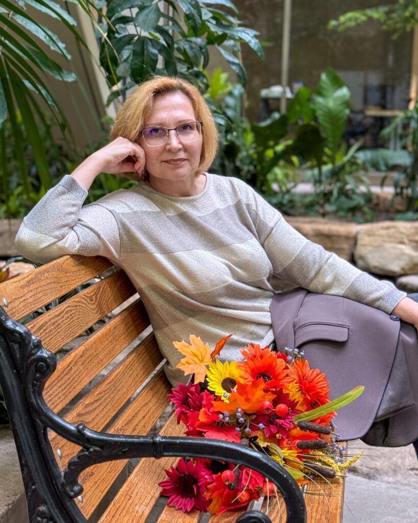 Olga Palamarenco sitting on a bench among plants, resting her chin on her hand.