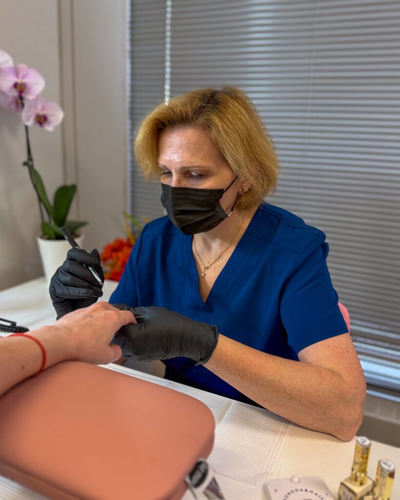 Olga Palamarenco, in a mask and gloves, working on a client's nails at the manicure table.