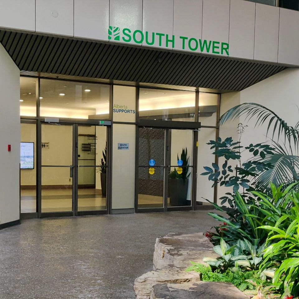 Glass doors under a green South Tower sign inside the building's atrium, with plants on the right.